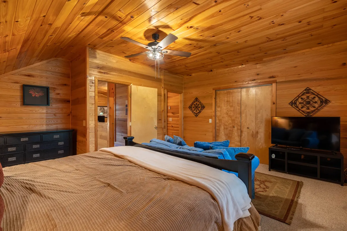 A spacious master suite featuring a king-sized bed with fresh bedding, a comfortable sofa, a large TV, and a wooden ceiling. The room feels warm and inviting, ideal for relaxation and privacy.