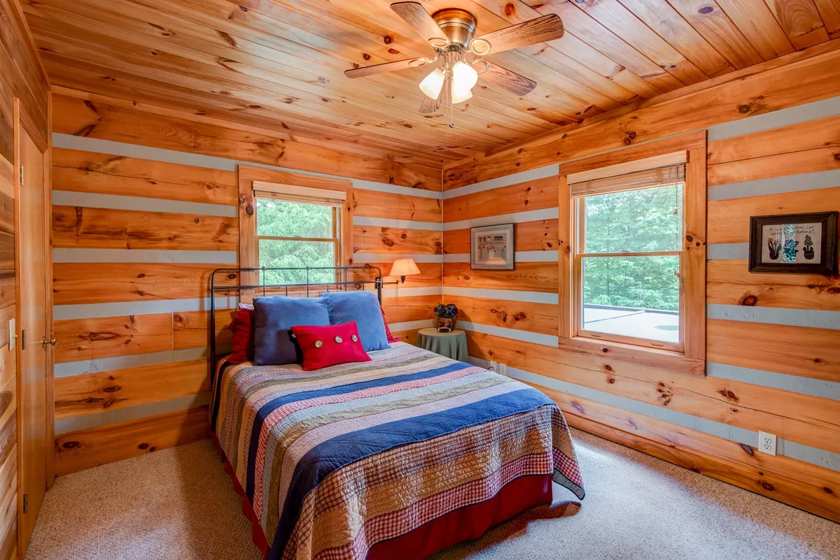 A bright bedroom with wooden walls, colorful bedding, and windows that overlook the surrounding natural landscape. The setting is peaceful and intimate, perfect for restful nights and waking up to mountain views and birdsong.