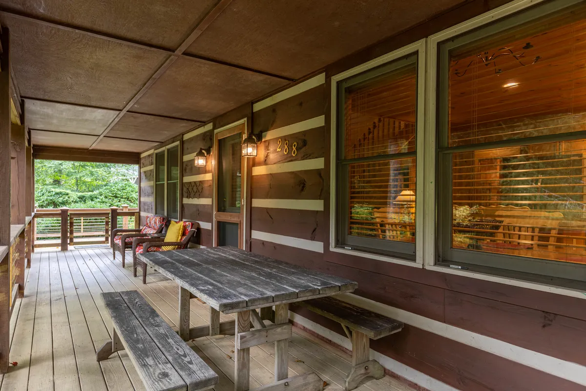 An inviting outdoor dining area with a wooden table, comfortable seating, decorative lanterns, and the log cabin structure visible. The scene is set for sunset dinners, morning coffee, or evening stargazing, all surrounded by natural beauty.