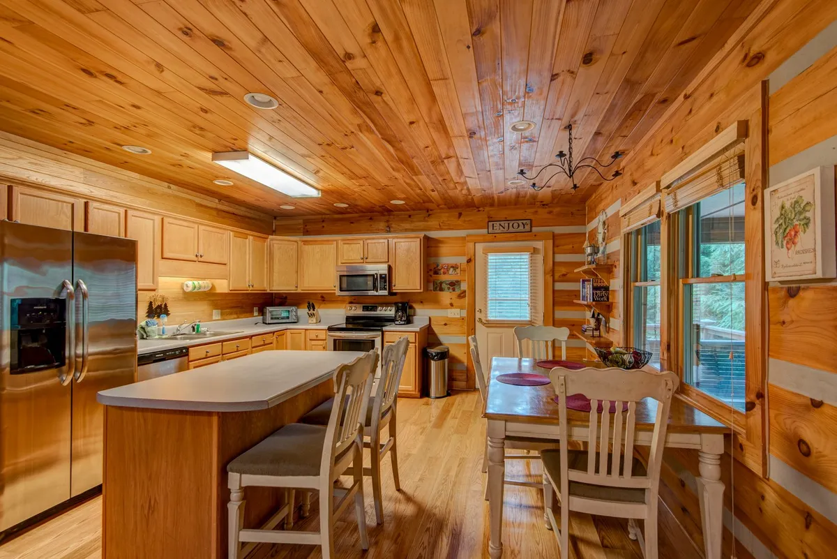 This image focuses on the fully equipped kitchen with its central island, stainless steel appliances, and wooden cabinetry. The adjacent dining table is visible, reinforcing the idea of shared meals and lively conversation.