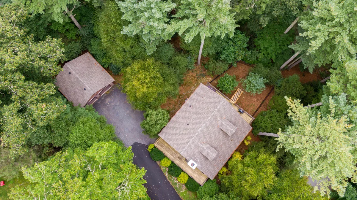 This image features the main house and guest house surrounded by mature trees, with a driveway leading up to the property. The tranquil setting highlights open outdoor space for relaxing, family gatherings, and outdoor exploration. The deck provides an inviting spot for watching sunsets and enjoying stargazing on clear nights.