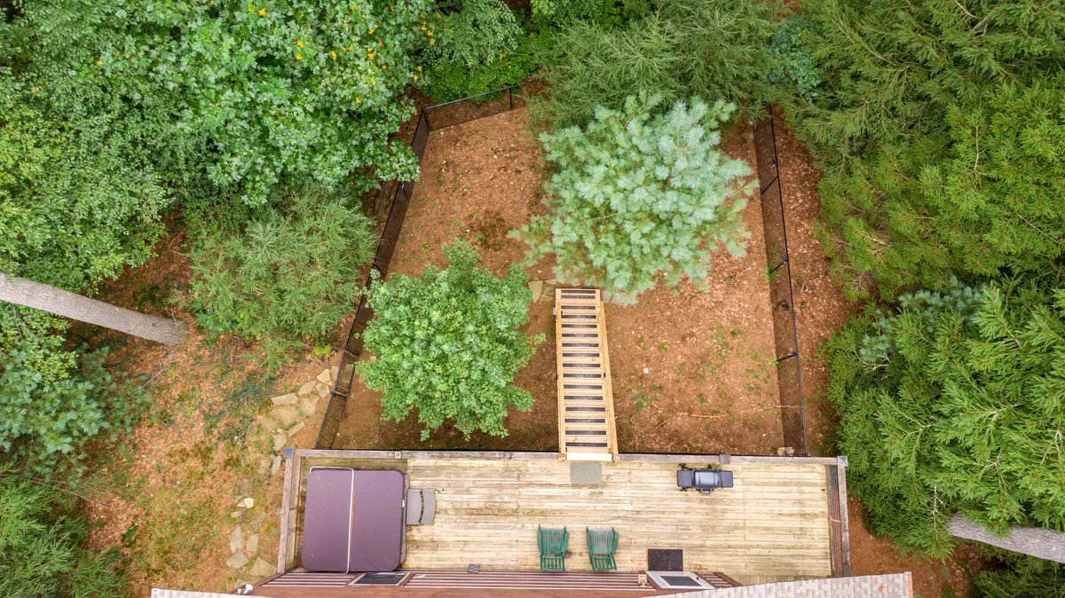 This image highlights another angle of the deck, showcasing a stairway leading down to the grounds, a hot tub nestled in the corner, and abundant green trees providing a serene, private setting.