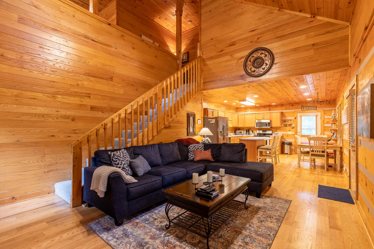This image offers a broader view of the living area, with a plush sofa, coffee table, staircase, and open sightlines into the kitchen. The arrangement suggests a seamless flow for entertaining and relaxation, connecting lounging and cooking spaces as described in the content.