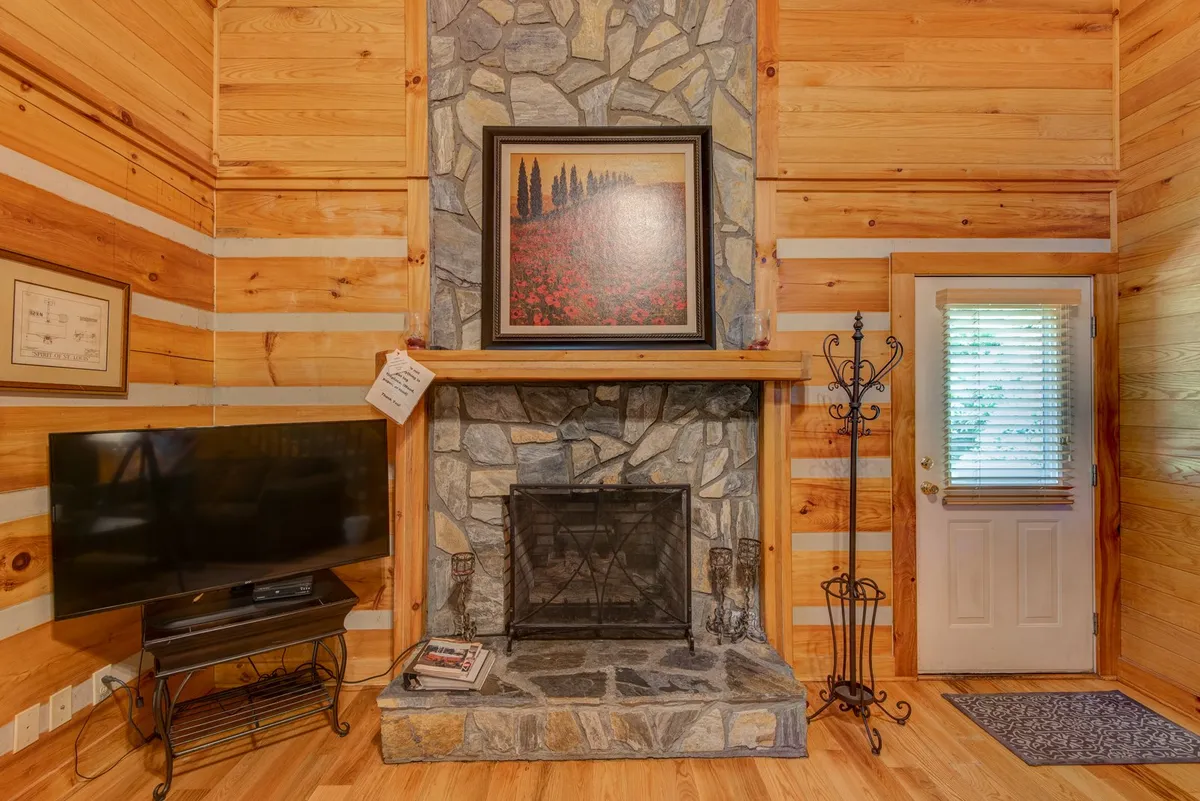 Inside the cabin, this scene focuses on a cozy stone fireplace framed by artwork and a television, set in a welcoming living area. The space exudes warmth and invites couples to relax by the fire, share stories, or enjoy a quiet evening together.